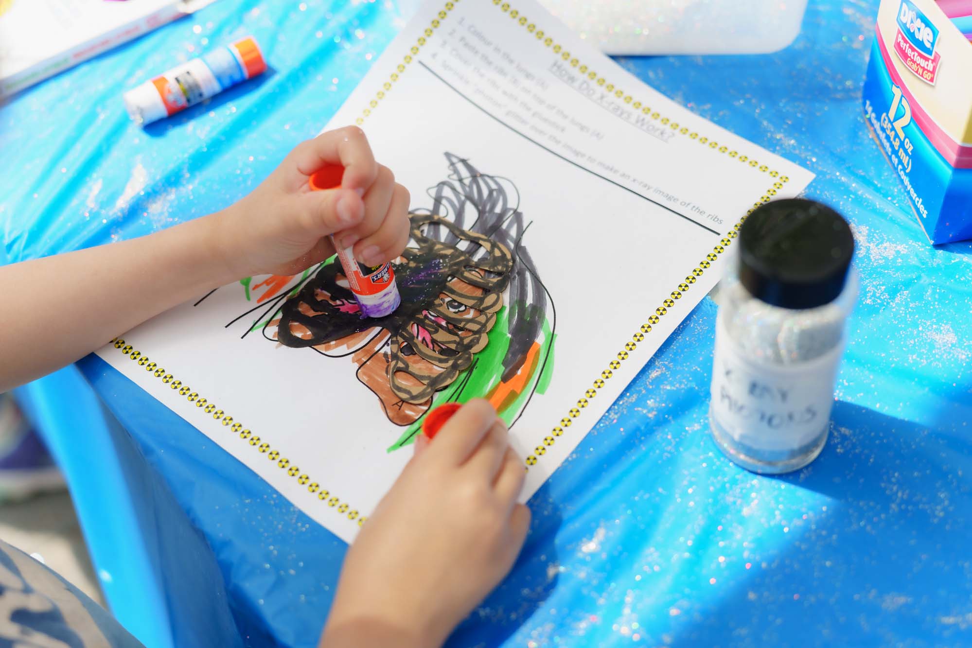 A child applying glue to the lung outlined on an activity worksheet with two glue sticks.