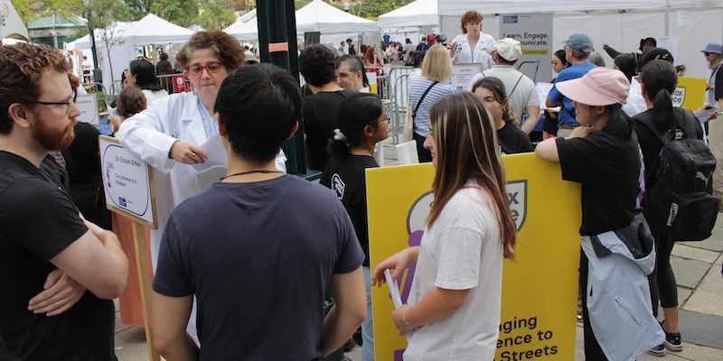 Crowded outdoor scene with tents, posters and many people listening to scientists speaking