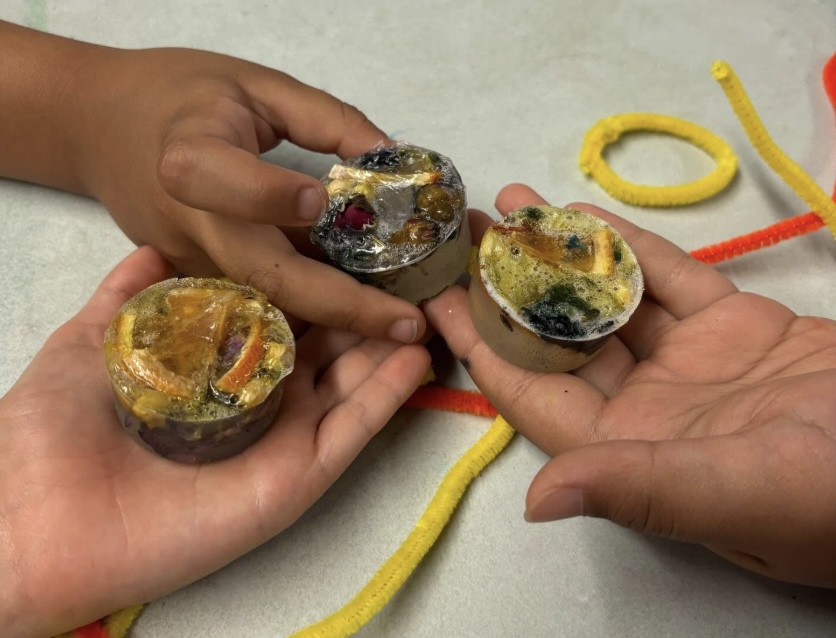 Three small hands. each displaying a round bar of soap they made with natural ingredients