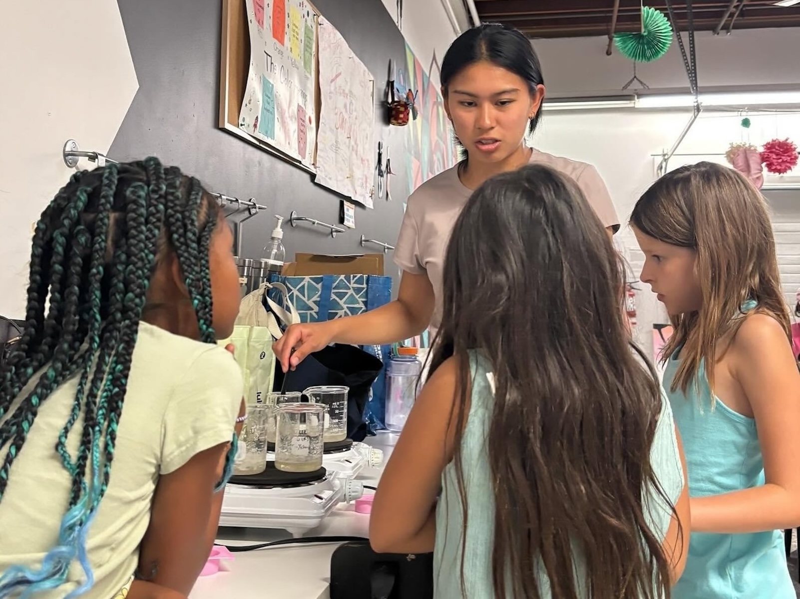 Three young girls watch instructor explain chemistry experiment with beakers on burners