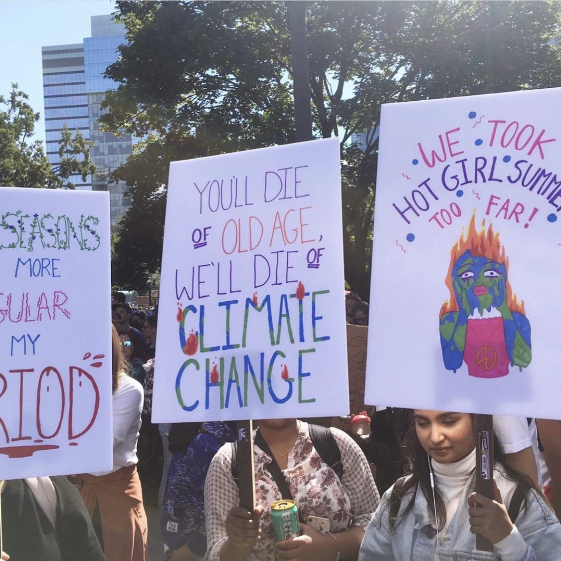 Young women holding up signs at a climate rally, one sign reads: You'll die of old age, we'll die of climate change.