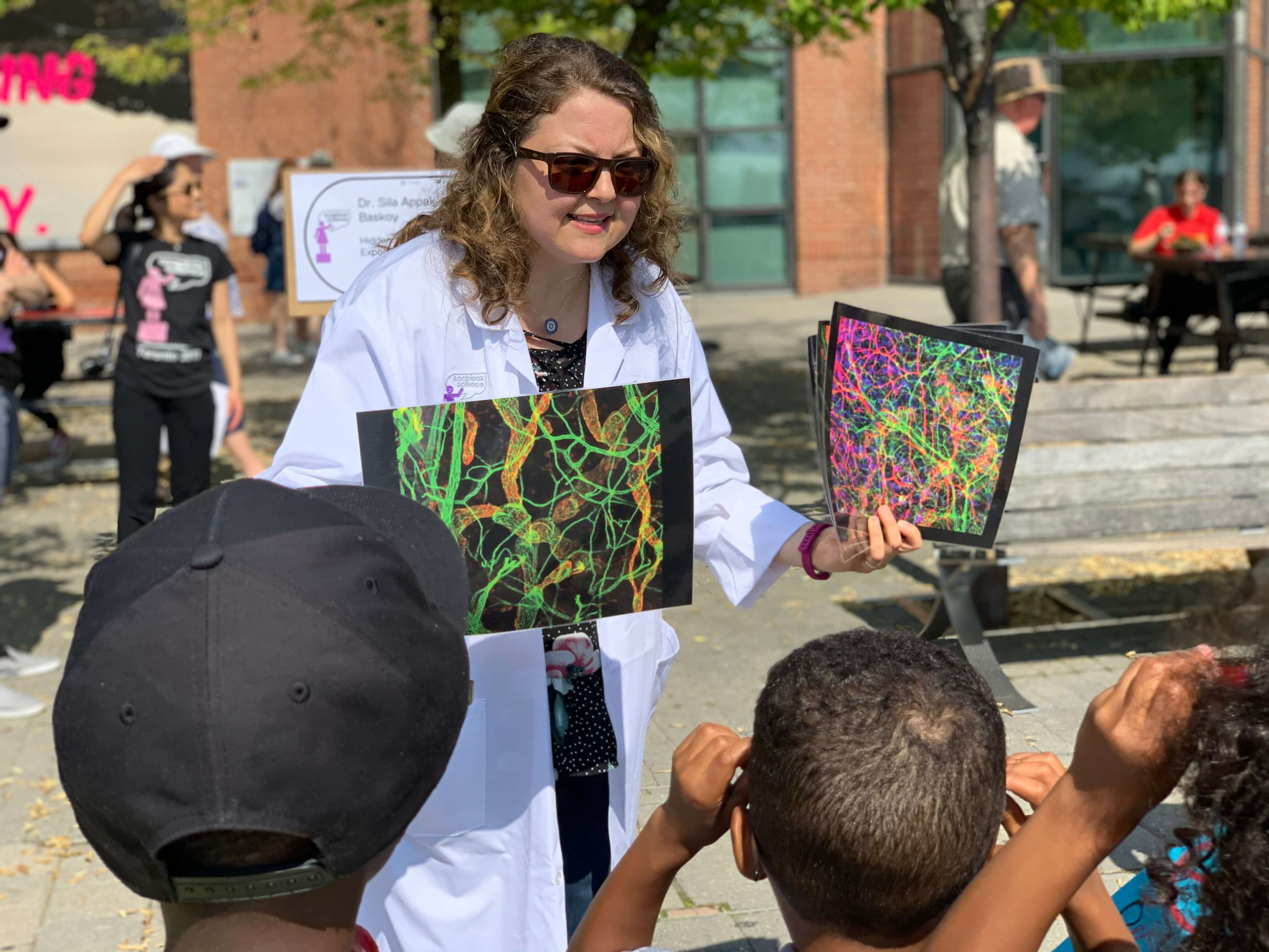 A female scientist is sunglasses and a lab coat showing colourful images of neural networks