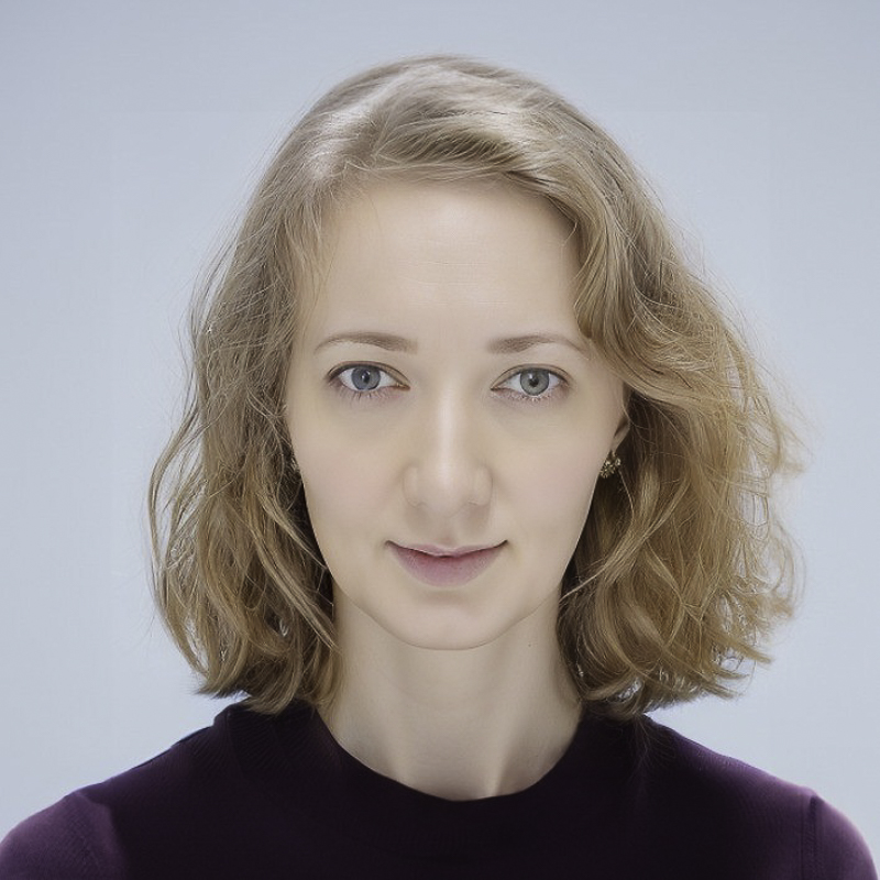 headshot of young woman with shoulder length blonde hair, blue eyes, wearing burgundy top