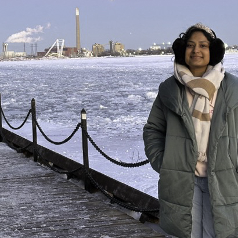 environmental portrait of young woman bundled up for winter weather, with icy landscape in the background, including smoke stack