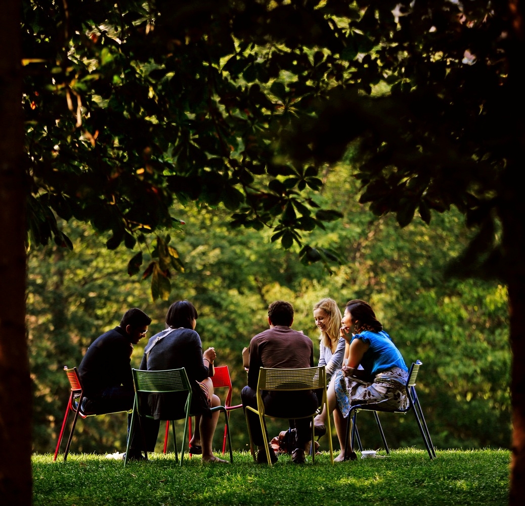 Group of people sitting on chairs in a circle outside, conversing