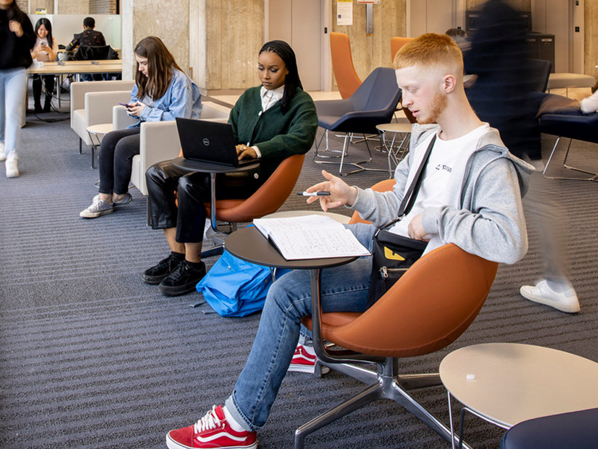 Three students sit at chairs studying in the Library.