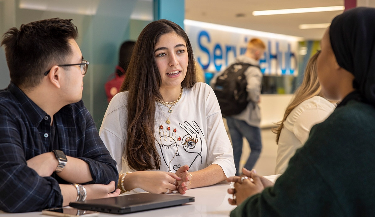 Two students speaking with an advisor in the ServiceHub. Other students can be seen in the background.