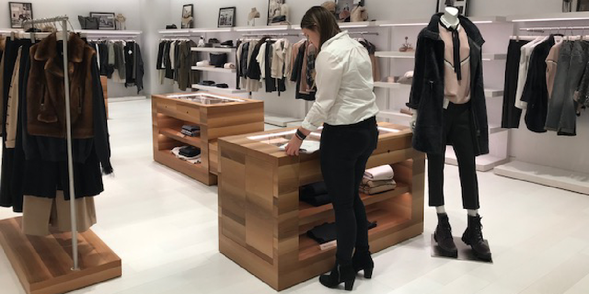 Person standing front of a wooden display box in a retail shop space with clothes around