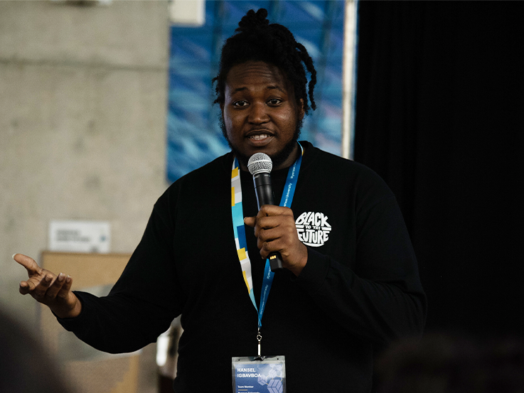 Student in black shirt and holding a microphone presenting to an audience.