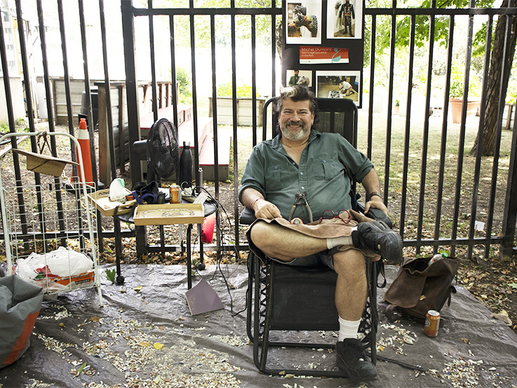 Man sitting in a black lawn chair surrounded by tile pieces and tools.