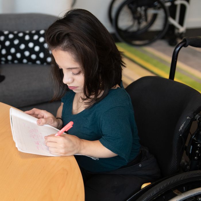 a woman in a wheelchair, writing in a notebook