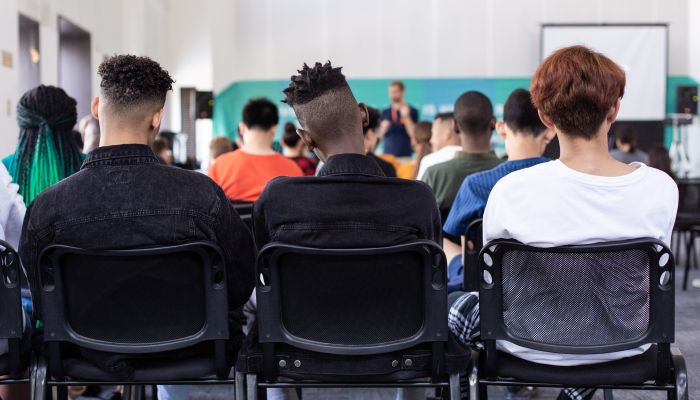 three young men sitting in chairs during a seminar, with their backs to the camera