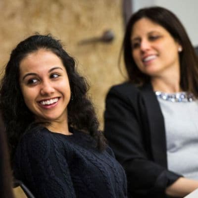Two white women sitting beside each other, smiling and leaning back in their chairs. They look relaxed. 