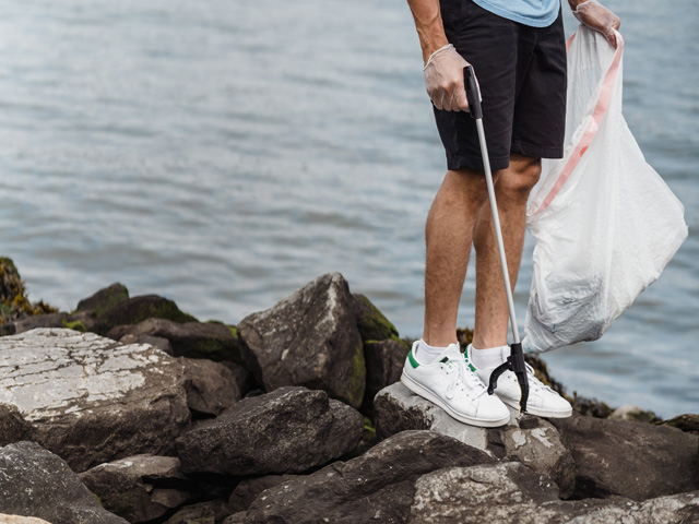 Human water steward cleaning up garbage along rocks at watershore.