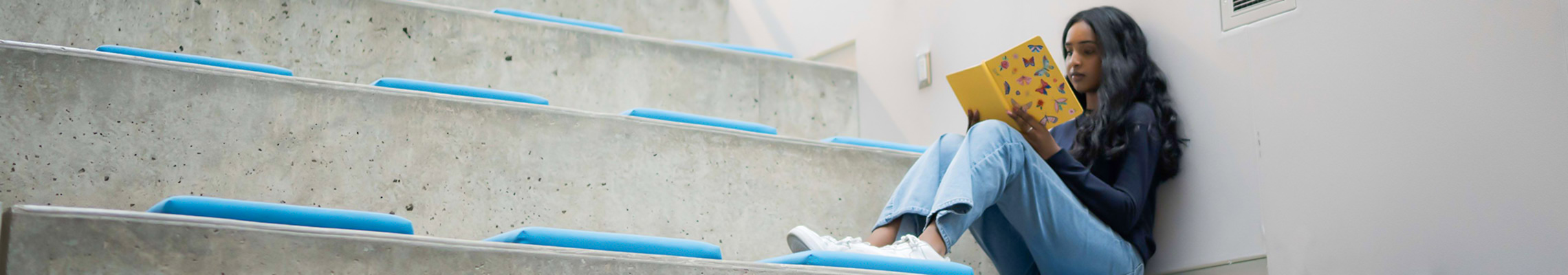 Student sits on steps of SLC reading textbook