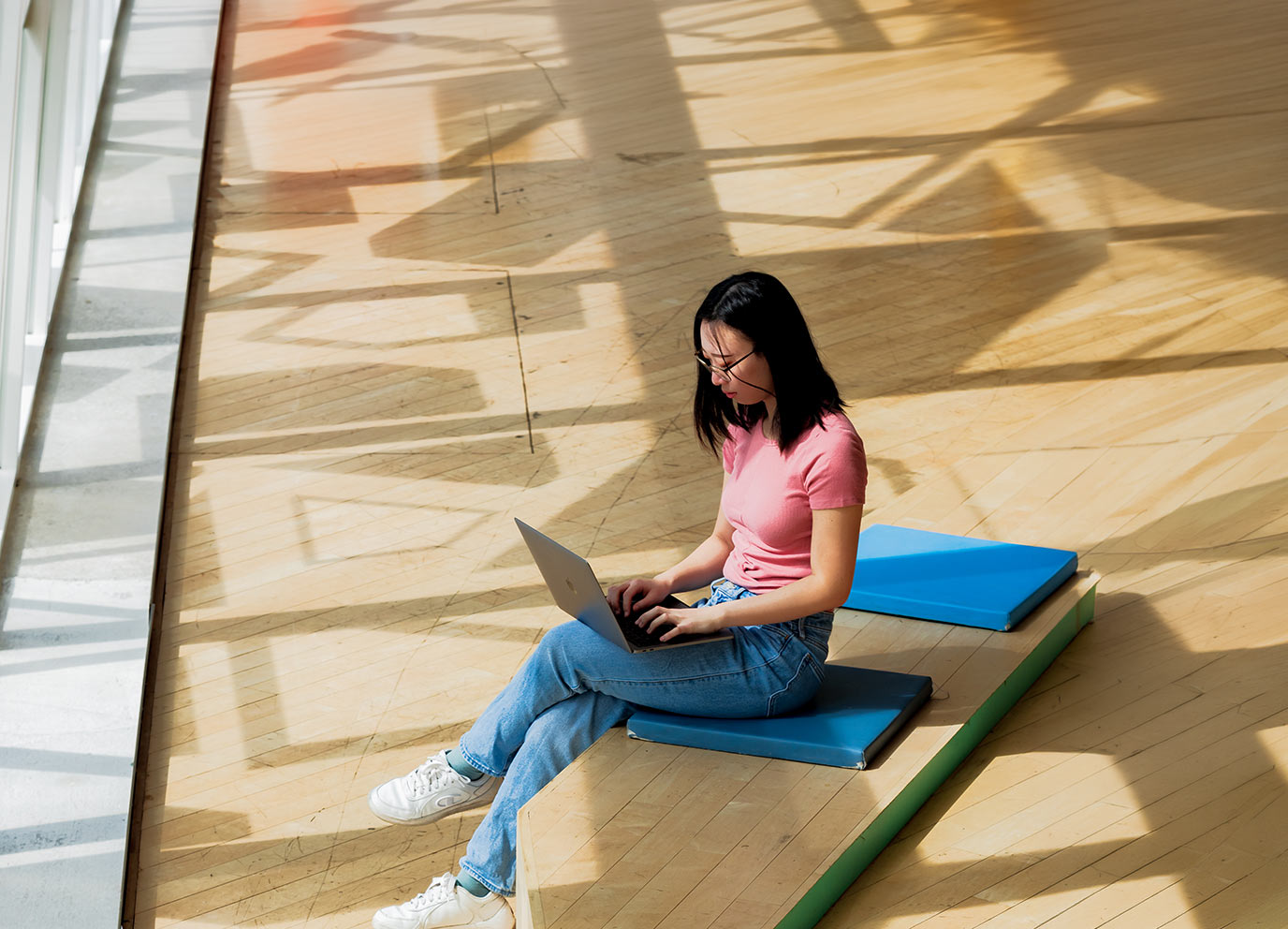 Student sits on a bench in the SLC at TMU working on a laptop