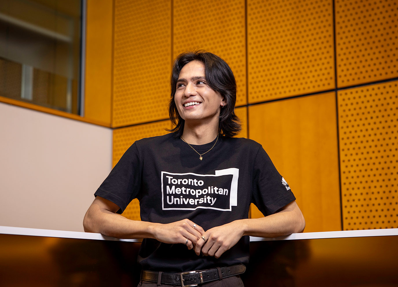 Student leaning against wall proudly wearing tshirt with Toronto Metropolitan University logo