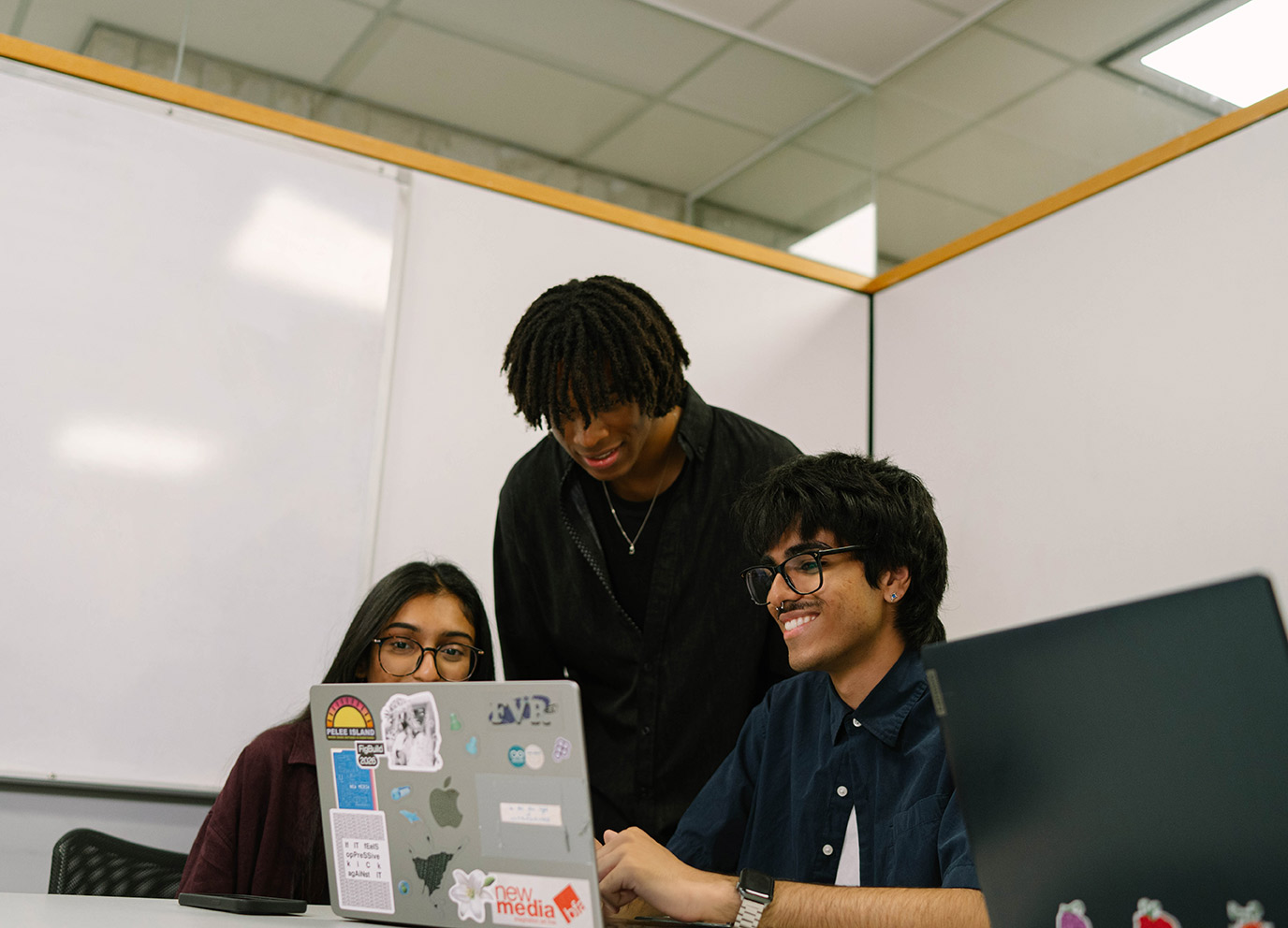 Three students on a computer together in a meeting room at TMU