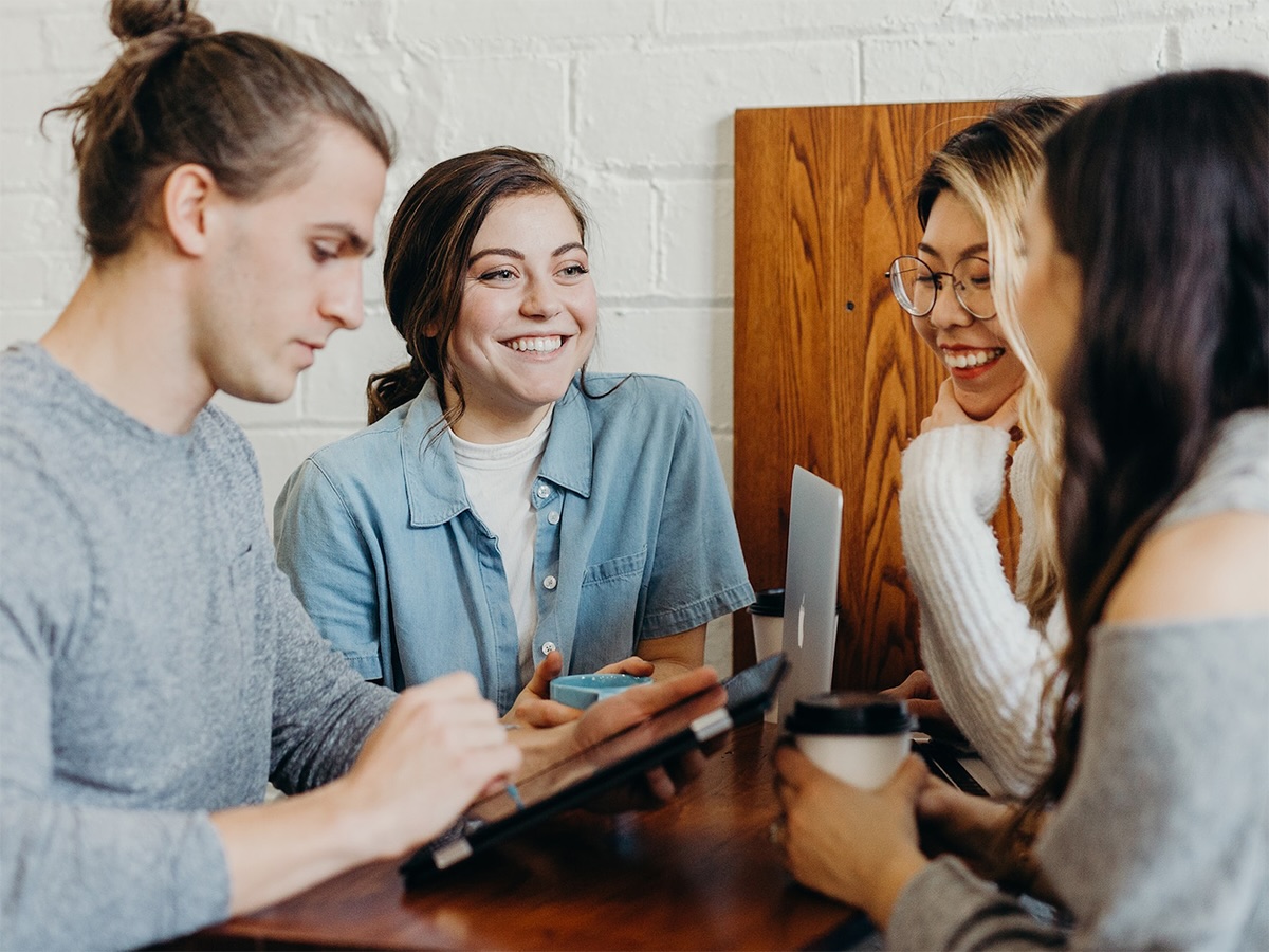 A group of students huddle around a table at a cafe talking and smiling.