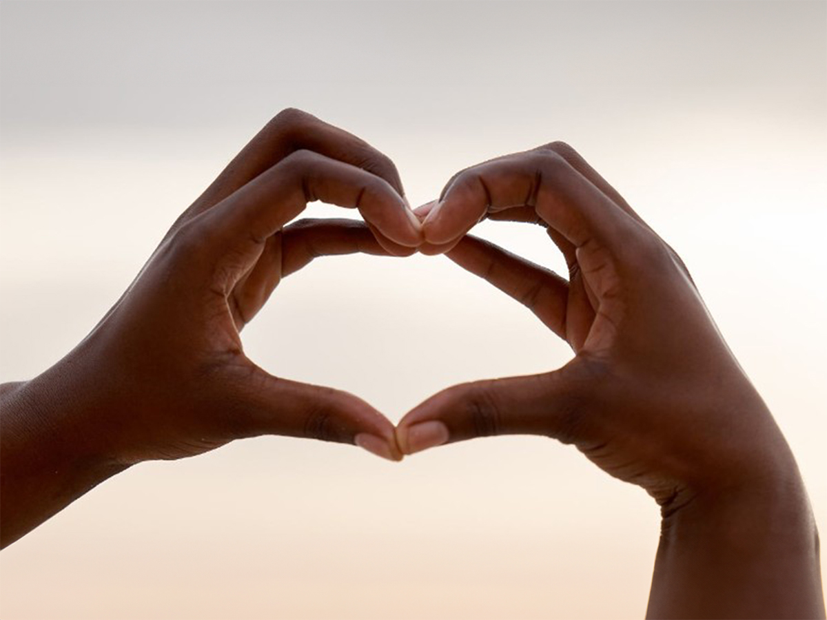 A pair of hands making the shape of a heart towards the sky.