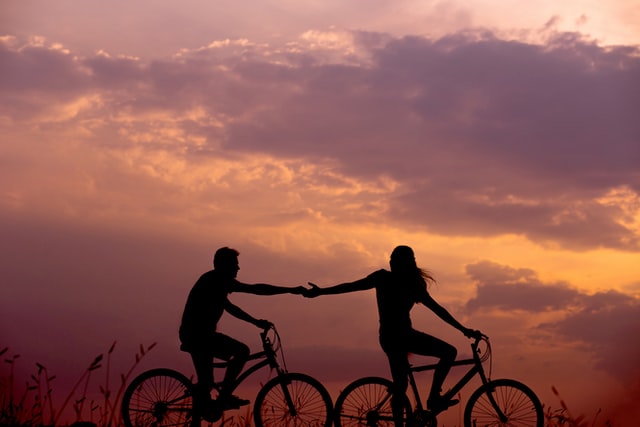 Two people riding bikes holding hands 