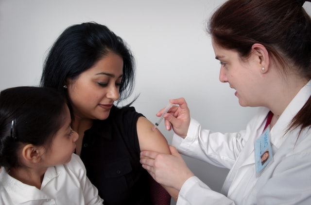 Woman receiving vaccination from doctor while daughter looks on