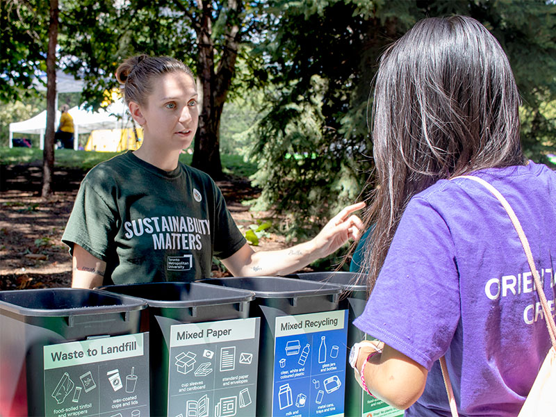 A student Sustainability Ambassador helps a ctudent learn what waste goes where at an Orientation event.