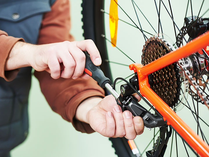 A technician's hands use a screwdriver to adjust a rear derailleur of a bicycle to help it shift smoothly through the gears.