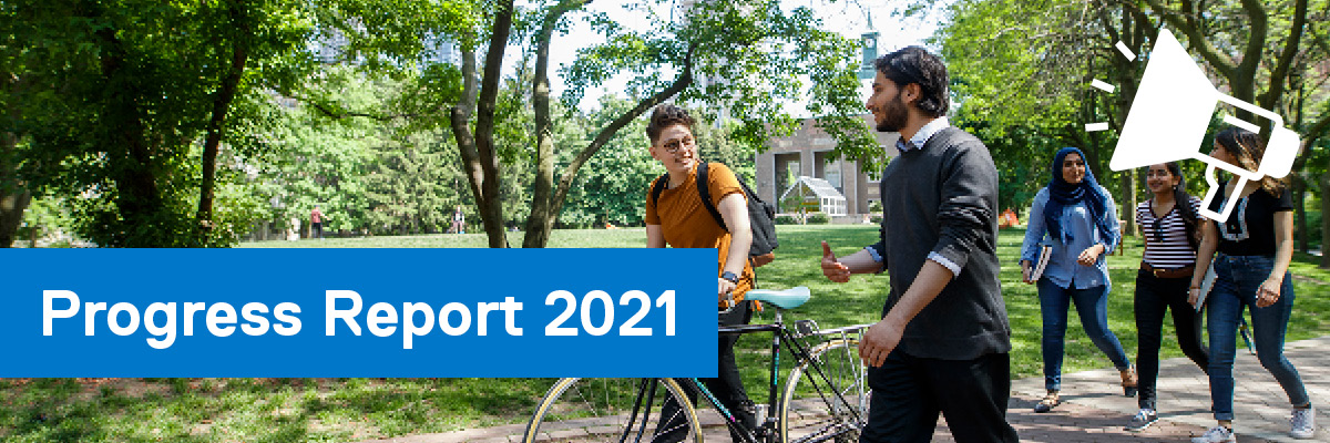 Five students walking through the lush green Quad, one of them with a bicycle.