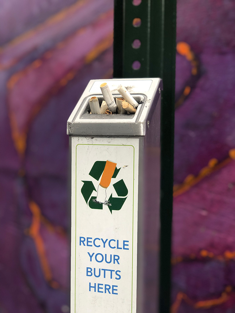 A cigarette butt receptacle mounted on a metal post.