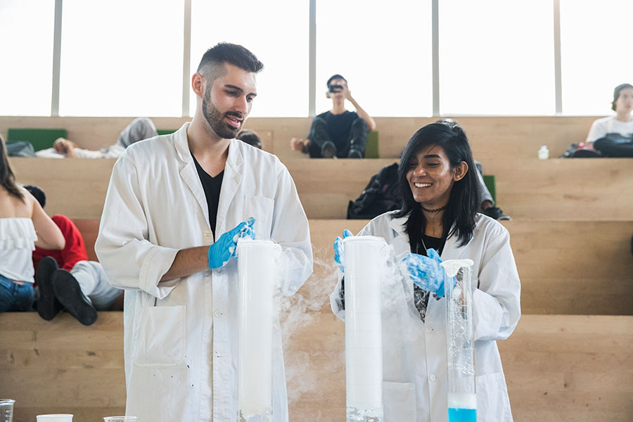 A male and a female student standing in front of three large vials in the SLC