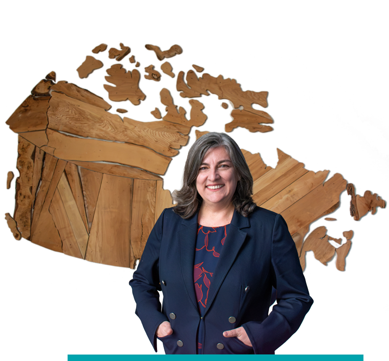 Dean Cynthia Holmes in a navy blazer stands in front of a wooden map of Canada