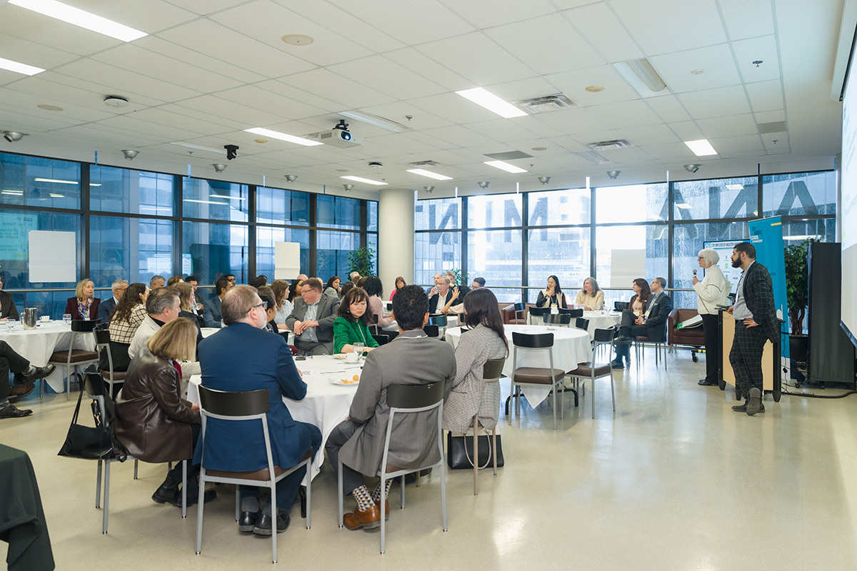 A diverse group of people attentively sit around tables at the advisory council meeting event. Mood is focused and engaged.