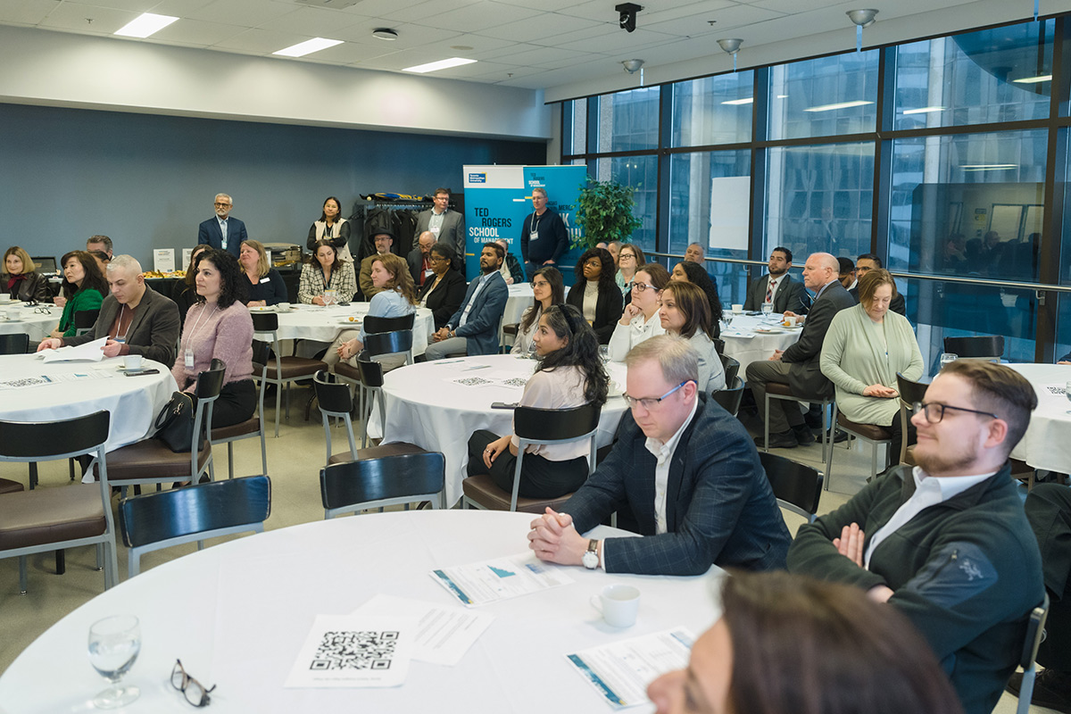 A diverse group of people attentively sit around tables at the advisory council meeting event. Mood is focused and engaged.