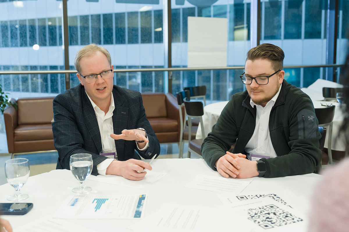 Two professionals engage in discussion around tables at the advisory council meeting. Alexander Lelievre leads the conversation.