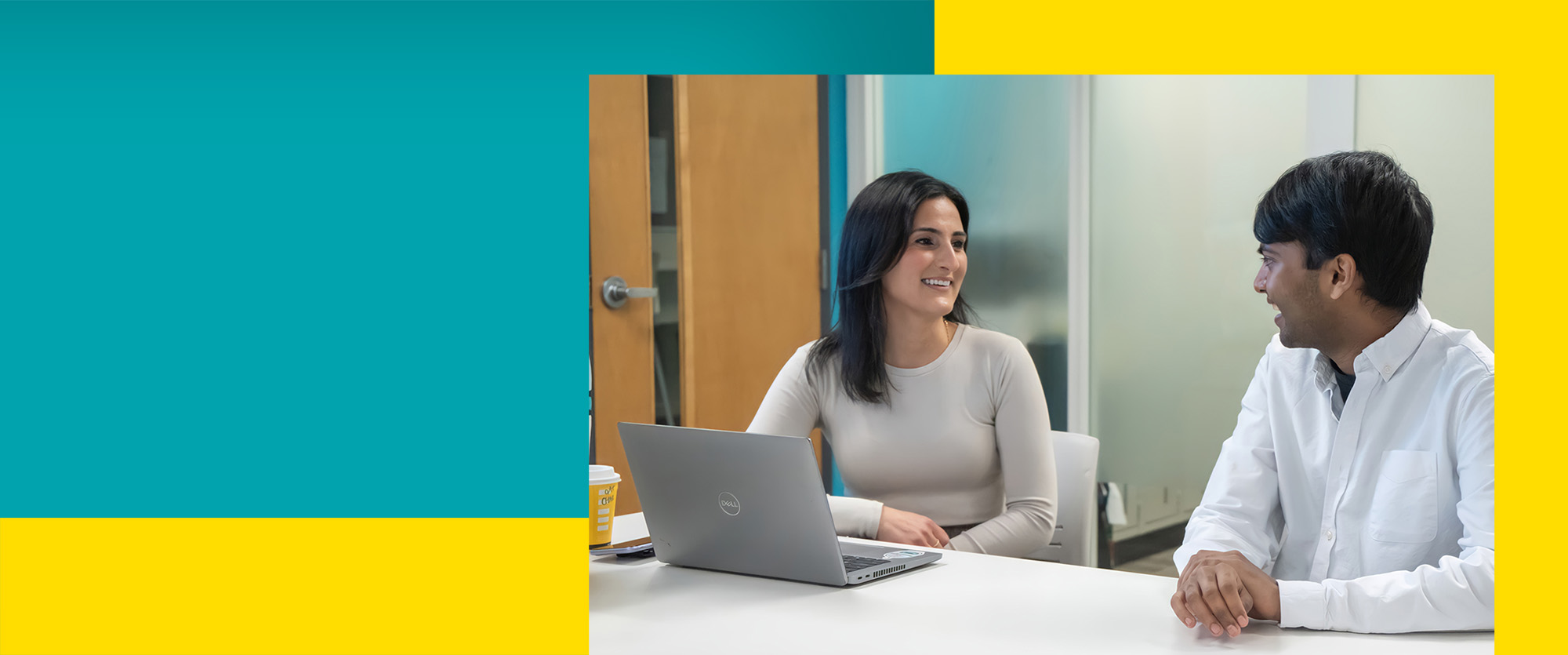 Two students meeting at a desk with a laptop on the desk
