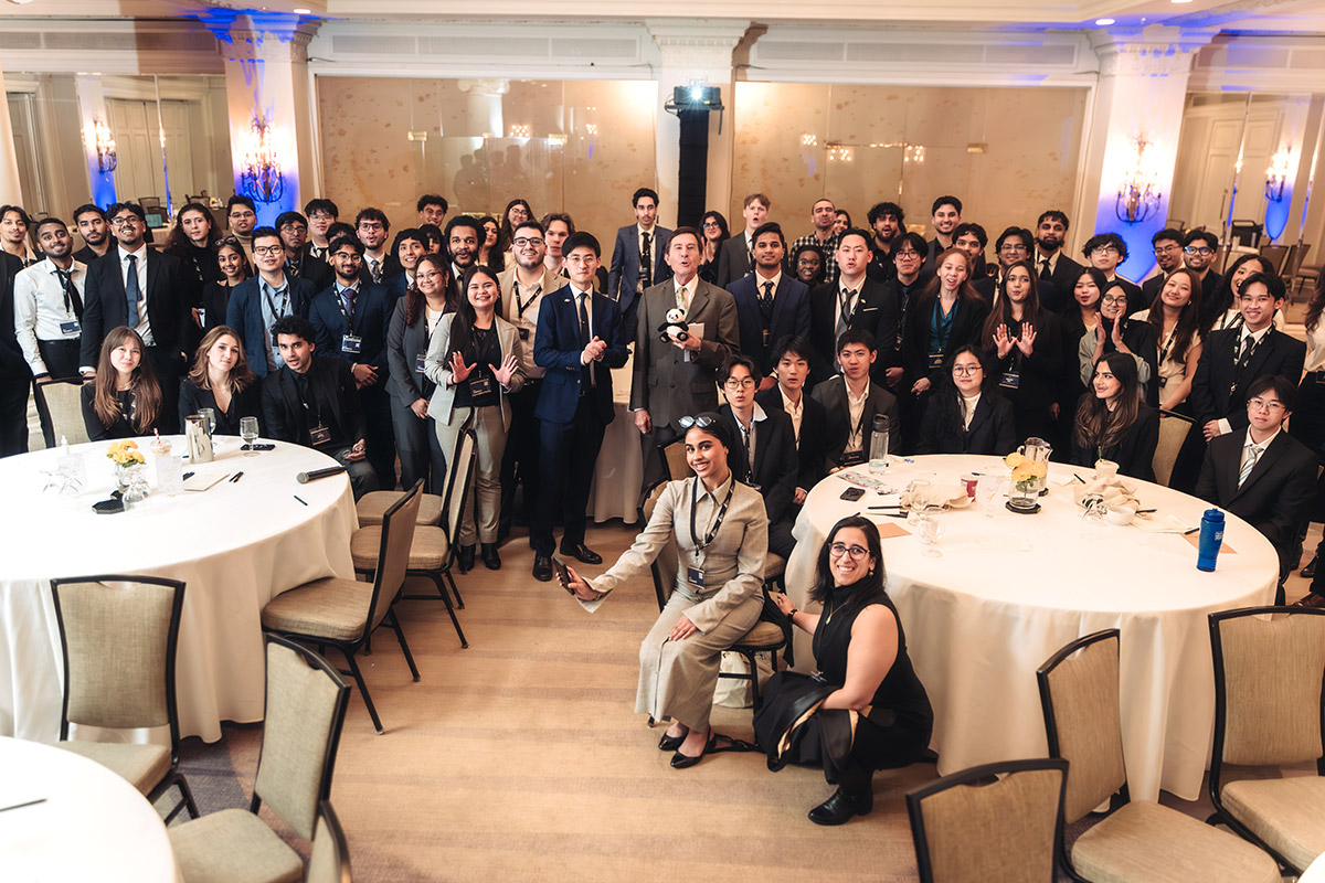 A very large group of diverse young professionals at a conference in a formal setting. They smile and face the camera, conveying a sense of camaraderie and optimism.