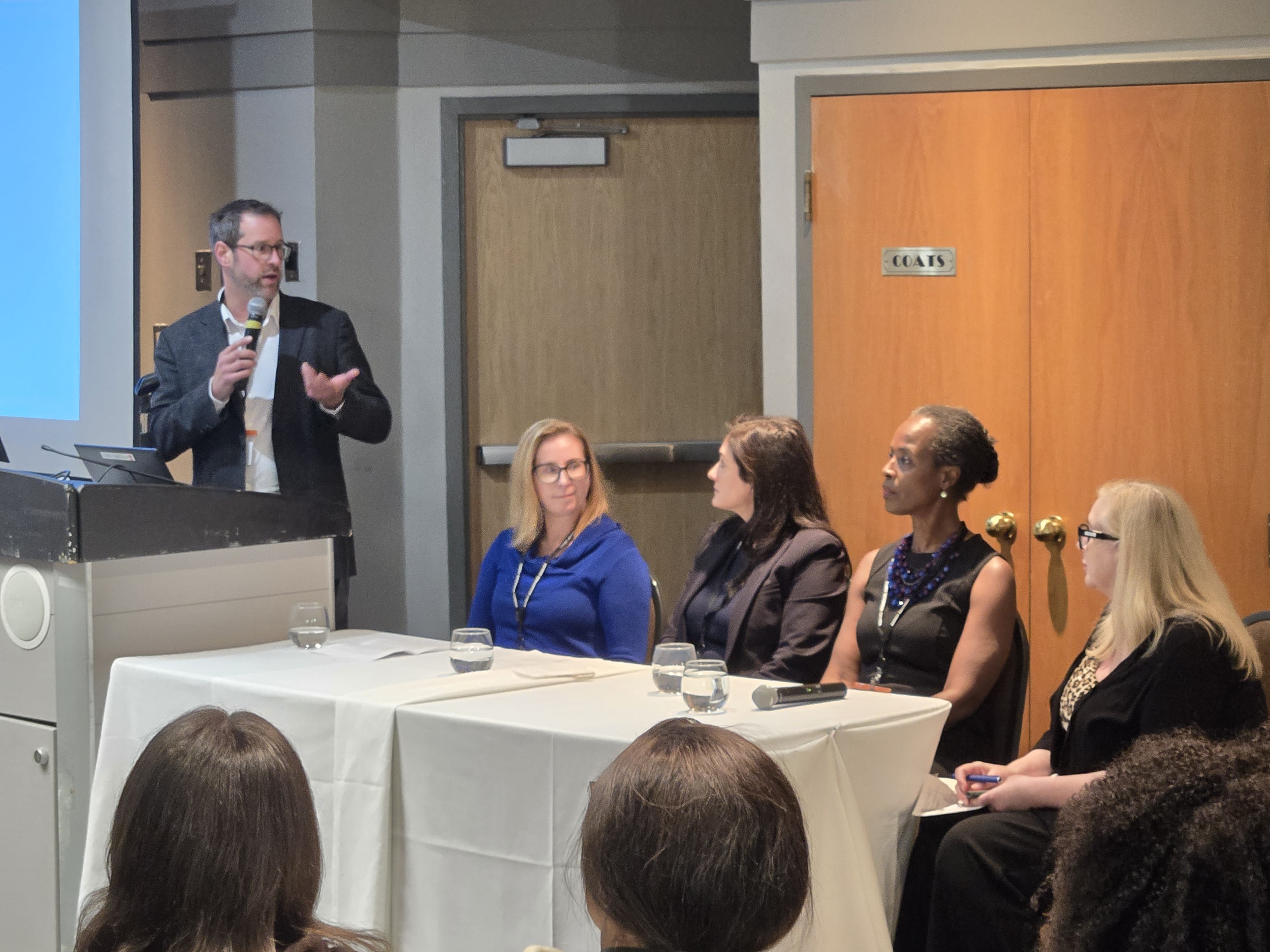 Steve Beauschene addresses the audience beside a seated panel during the Family Business event.