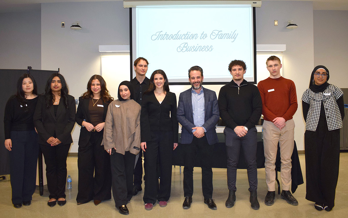 Professor Francesco Barbera with a diverse group of nine FBSA students stands smiling in front of a projection screen that reads "Introduction to Family Business." They display a welcoming and professional tone.