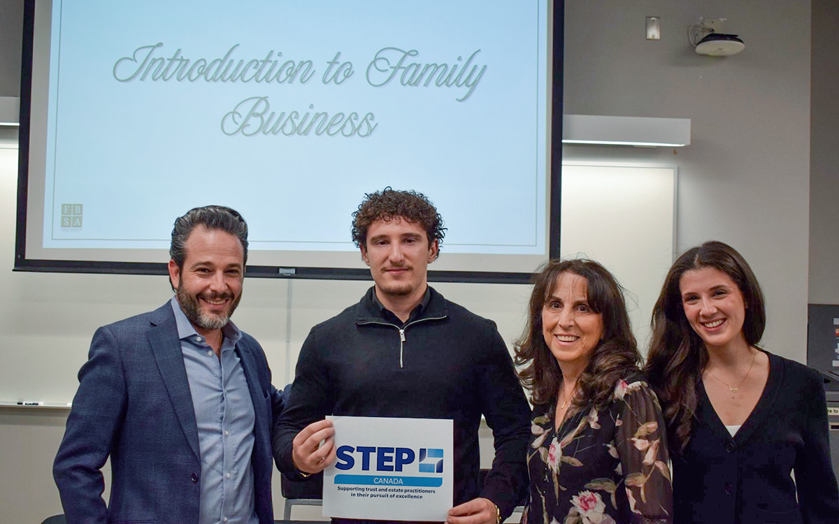 Family Business Institute team with award recipient, Nicolas, stand smiling in front of a screen displaying "Introduction to Family Business" in a classroom. Nicolas Fortuna holds a STEP Canada certificate.