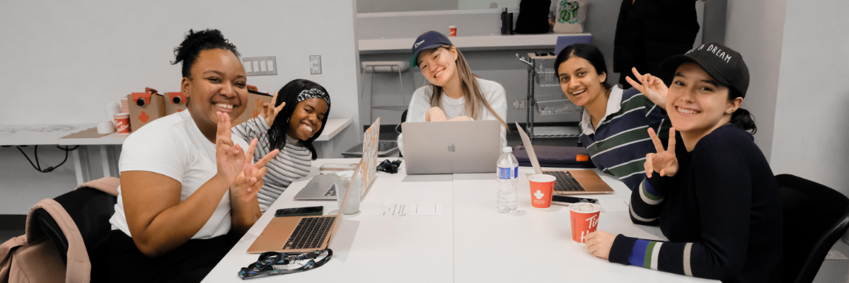 Students sitting at a table with laptops smiling