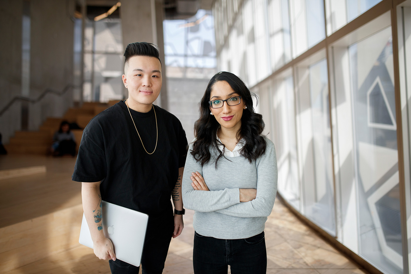 Two diverse students standing side by side and one is holding a laptop and smiling at the camera