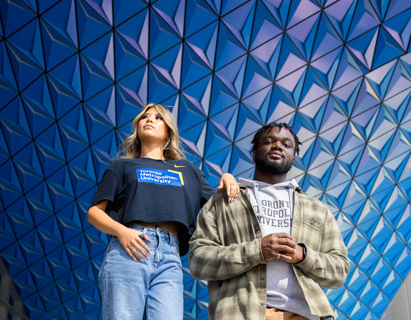Two diverse TMU students, one looking up and the other looking down at the camera with a dark blue background