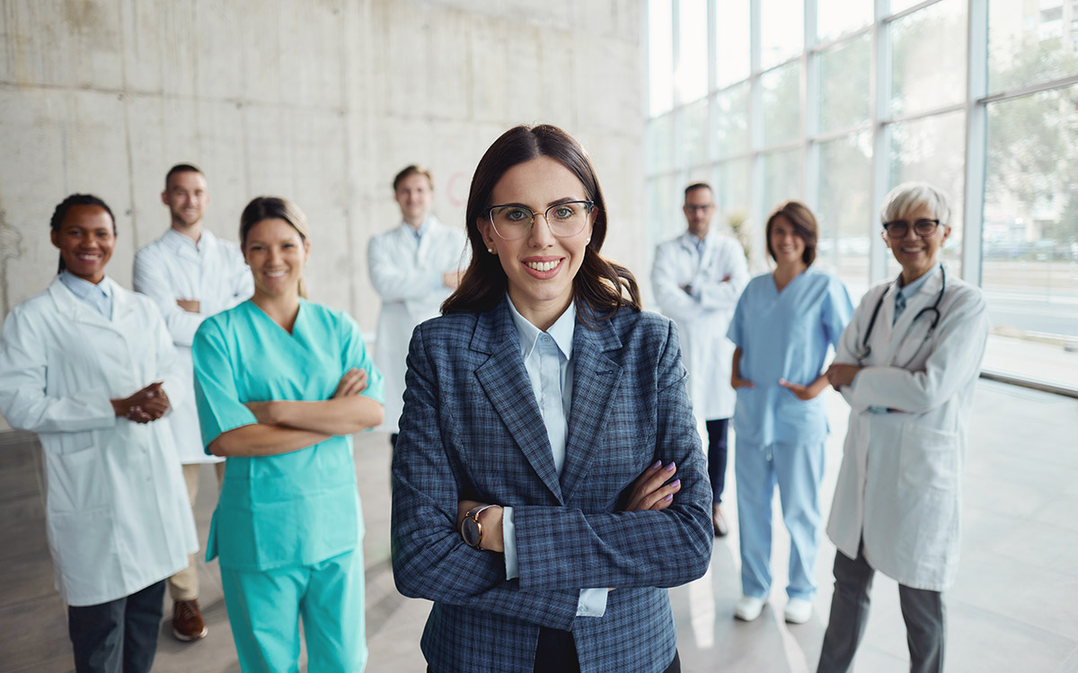Businesswoman standing in front of group of healthcare professionals with crossed arms and looking at camera