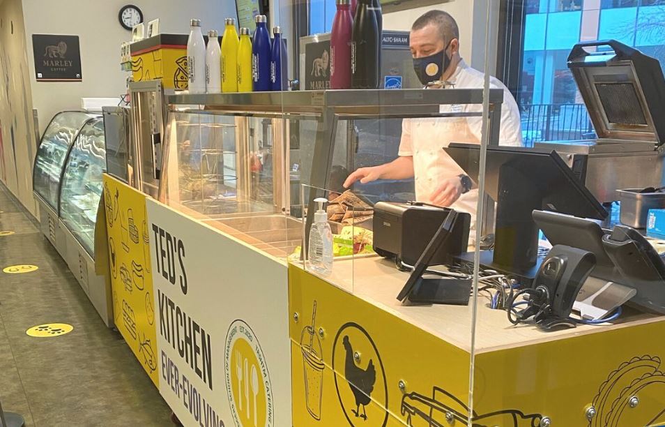 Ted's Kitchen kiosk. A man is working behind the kiosk with a mask on.