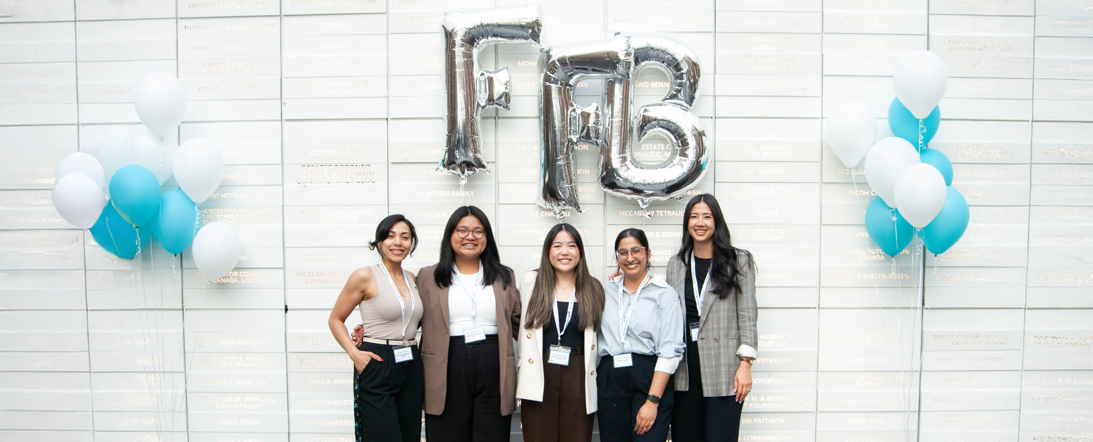 Staff and students standing a donor wall with large letter balloons at the Fit For Business celebration