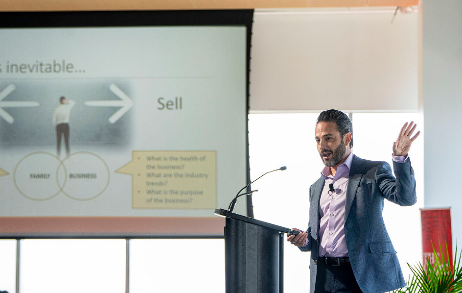 Francesco Barbera stands behind a podium in front of a screen showing a slideshow.