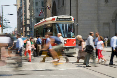 A busy street with people crossing the road in front of a parked ttc streetcar in the middle of letting off passengers and welcoming new ones