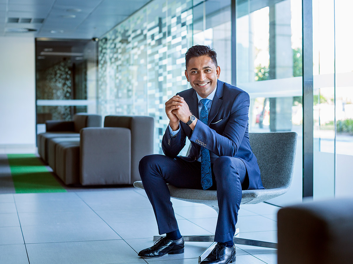 Full length portrait of happy businessman sitting with hands clasped in office lobby