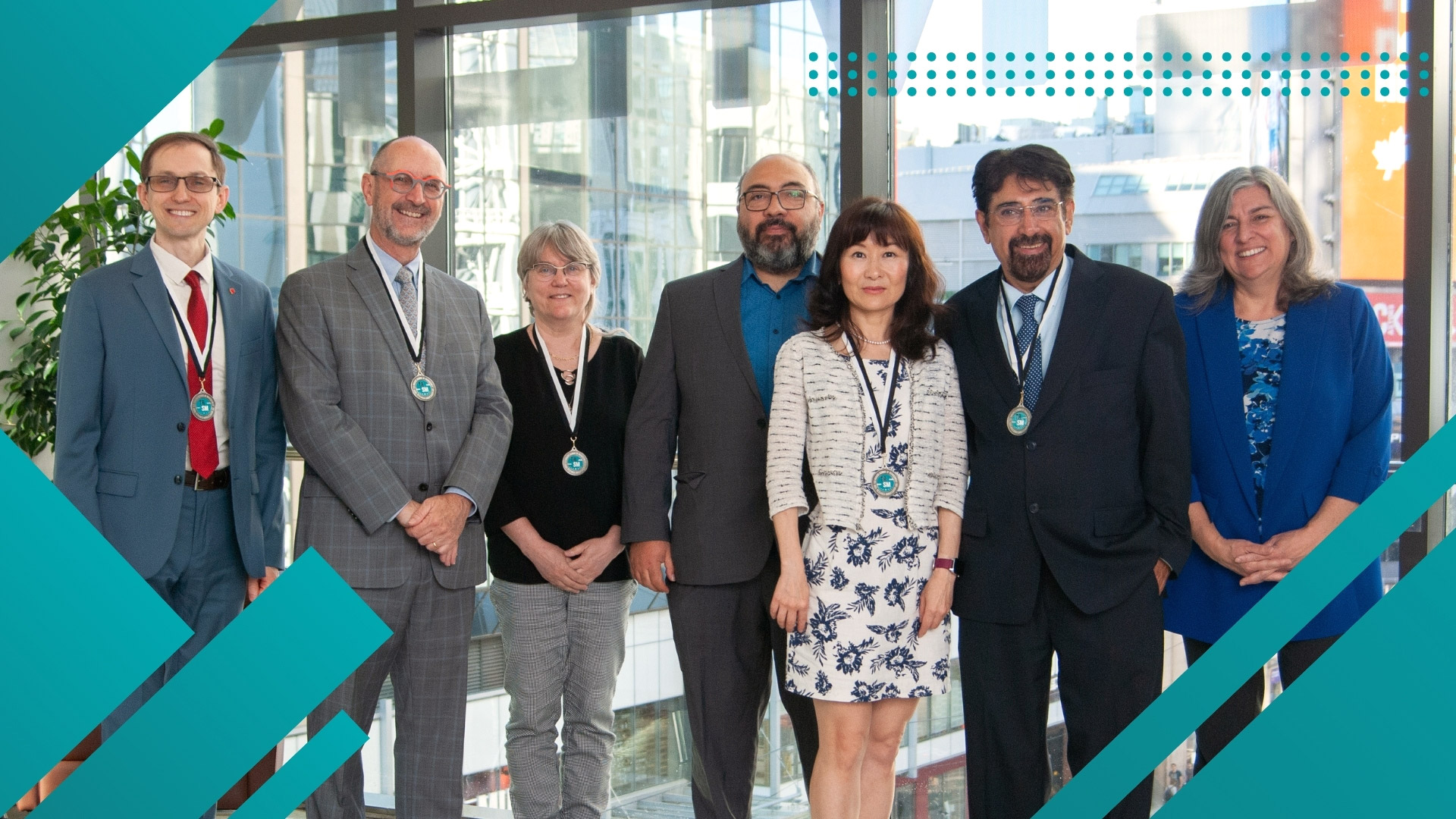 A group of eight faculty members stand smiling, each wearing a medallion at the Ted Rogers School of Management building